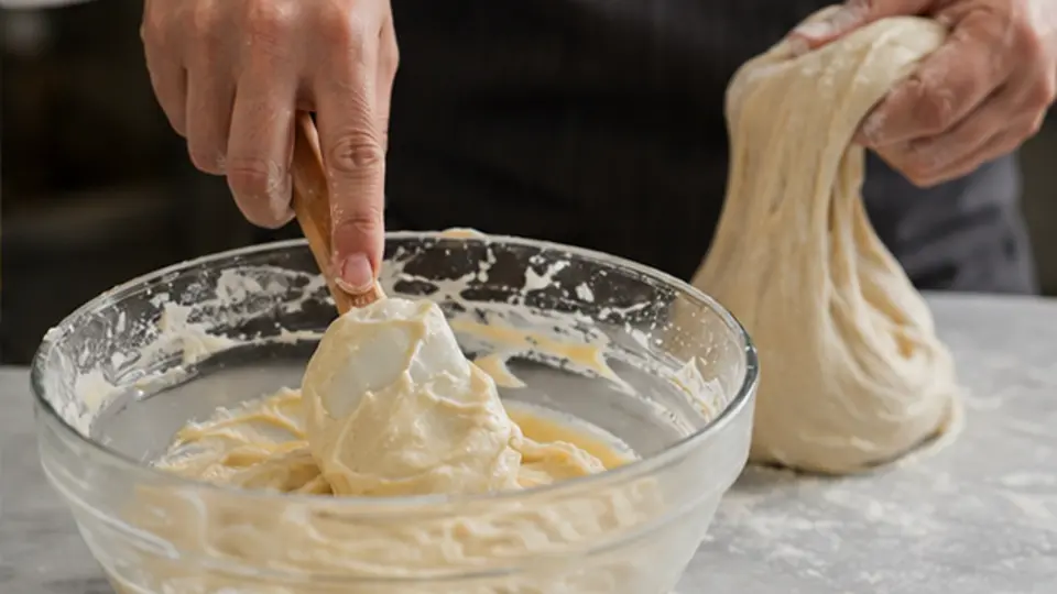 Pastry chef folding batter beside an elastic developed dough at a professional station